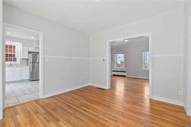 spare room featuring visible vents, a sink, radiator heating unit, light wood-style floors, and baseboards