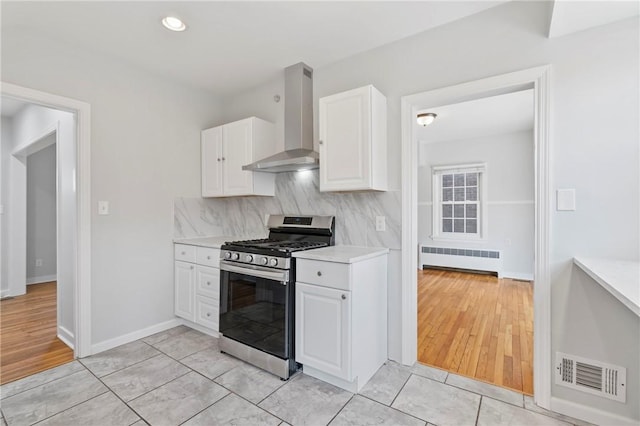 kitchen featuring radiator, visible vents, light countertops, stainless steel gas range oven, and wall chimney exhaust hood