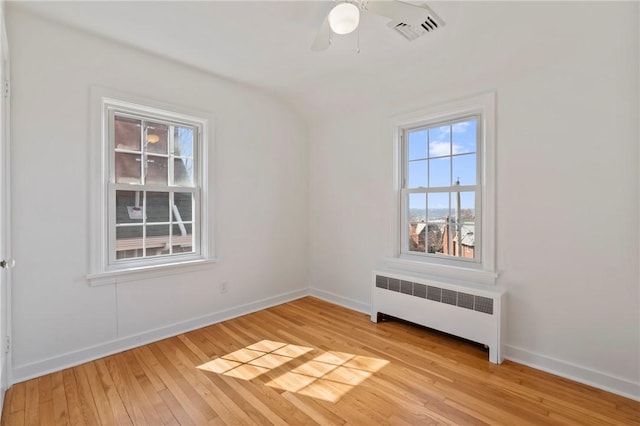 spare room featuring light wood finished floors, visible vents, ceiling fan, baseboards, and radiator heating unit