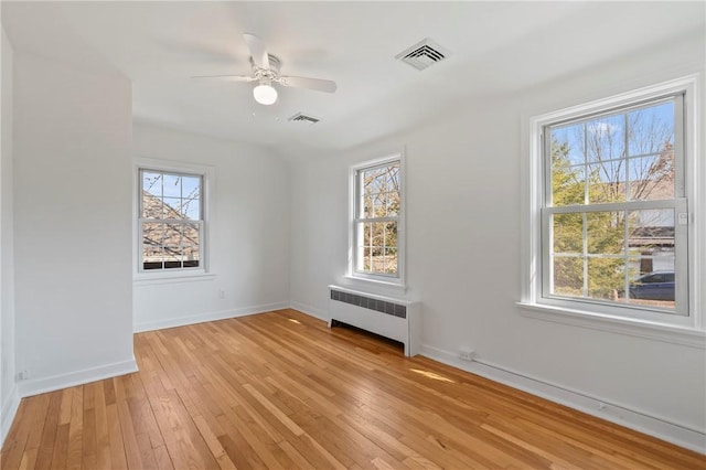 empty room with visible vents, radiator, light wood-type flooring, and baseboards