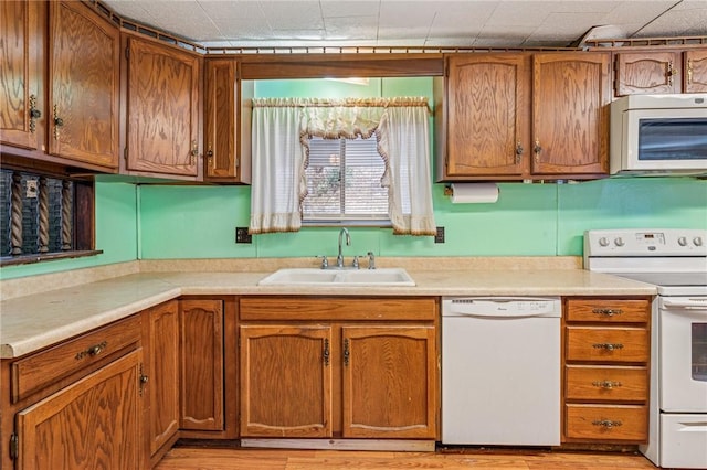 kitchen featuring white appliances, brown cabinetry, and a sink