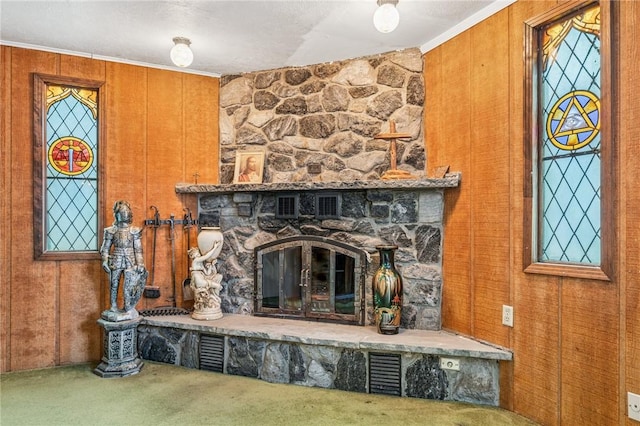 interior details with wooden walls, visible vents, ornamental molding, a stone fireplace, and carpet flooring