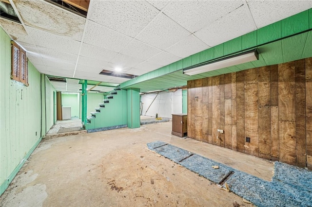 finished below grade area featuring stairway, wooden walls, and a drop ceiling