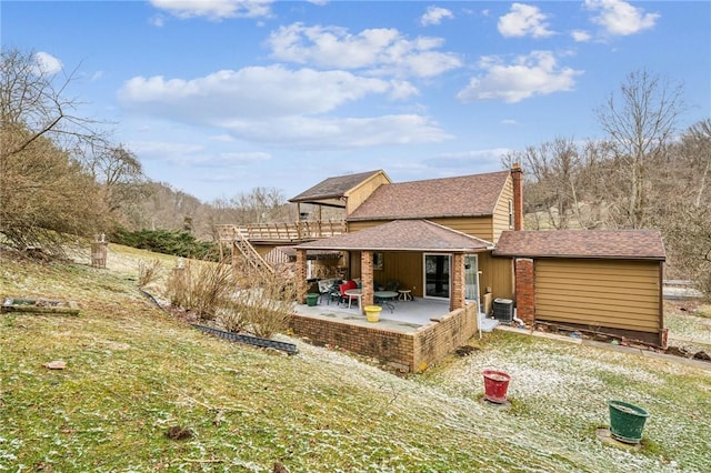 rear view of property with central AC unit, a chimney, a patio, and roof with shingles