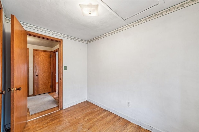 empty room featuring attic access, baseboards, and light wood finished floors