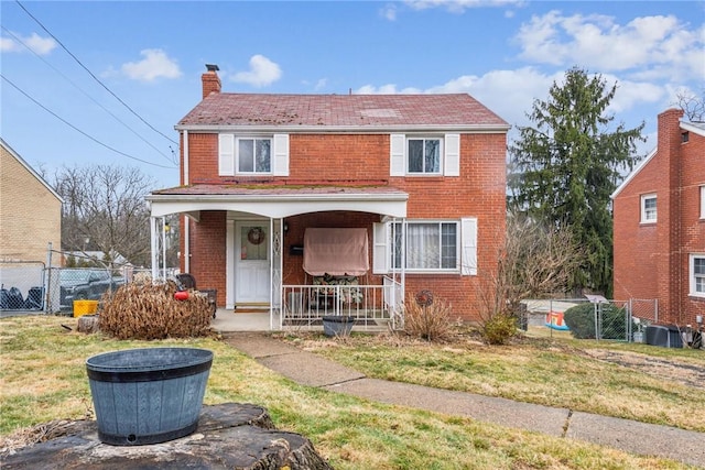 view of front of house with brick siding, a front lawn, covered porch, a chimney, and a gate