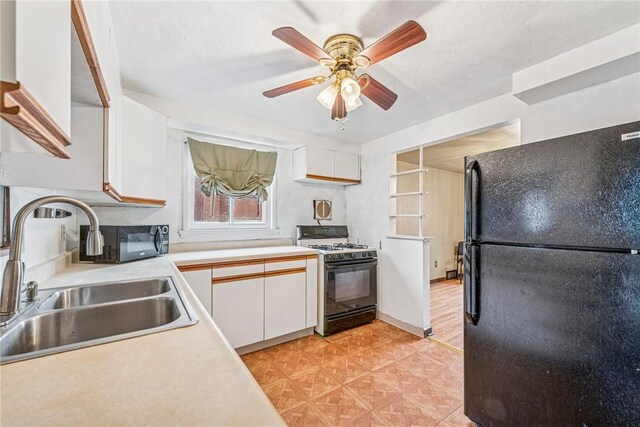 kitchen featuring gas range, light countertops, freestanding refrigerator, white cabinetry, and a sink