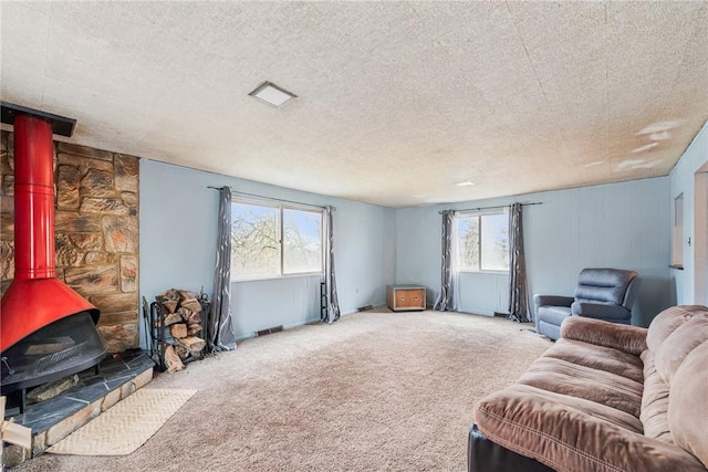 carpeted living area with a wood stove, visible vents, and a textured ceiling