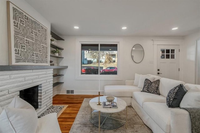 living area with wood finished floors, visible vents, baseboards, recessed lighting, and a brick fireplace