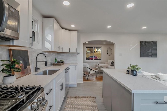 kitchen with arched walkways, a sink, stainless steel appliances, light countertops, and white cabinetry