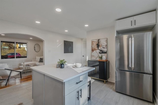 kitchen with a center island, light countertops, freestanding refrigerator, arched walkways, and white cabinetry