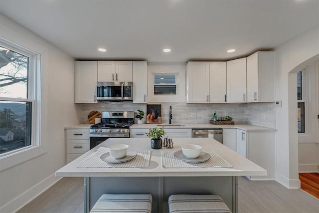 kitchen with a sink, white cabinetry, appliances with stainless steel finishes, light countertops, and decorative backsplash