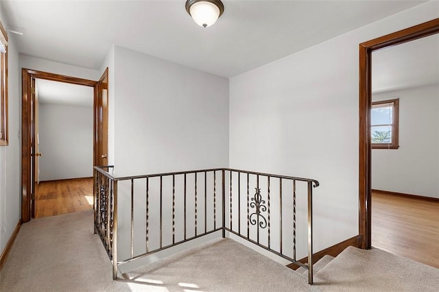 corridor featuring baseboards, an upstairs landing, and wood finished floors