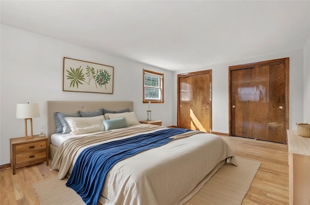 bedroom with light wood finished floors, two closets, and baseboards