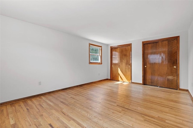 unfurnished bedroom featuring baseboards, multiple closets, and light wood-style flooring