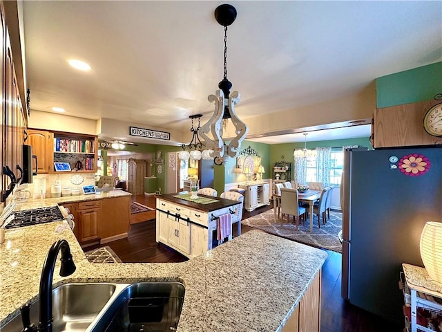 kitchen featuring light stone countertops, a kitchen island, a sink, hanging light fixtures, and stainless steel appliances