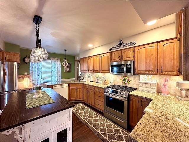 kitchen with a peninsula, light stone counters, tasteful backsplash, and appliances with stainless steel finishes