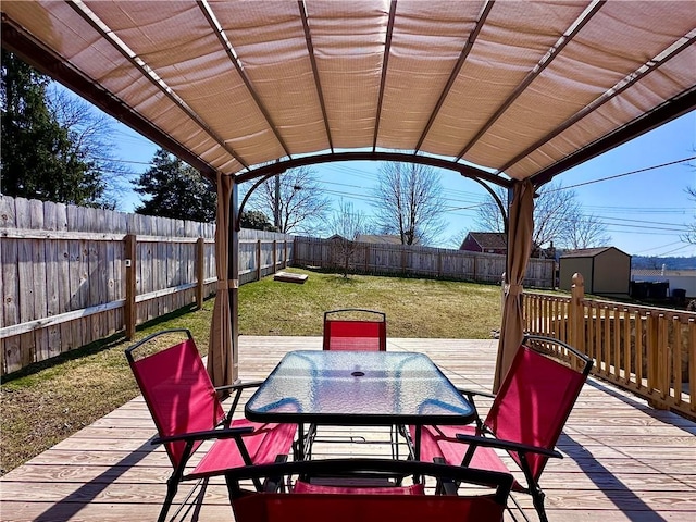 deck with a shed, a yard, an outdoor structure, a fenced backyard, and outdoor dining space