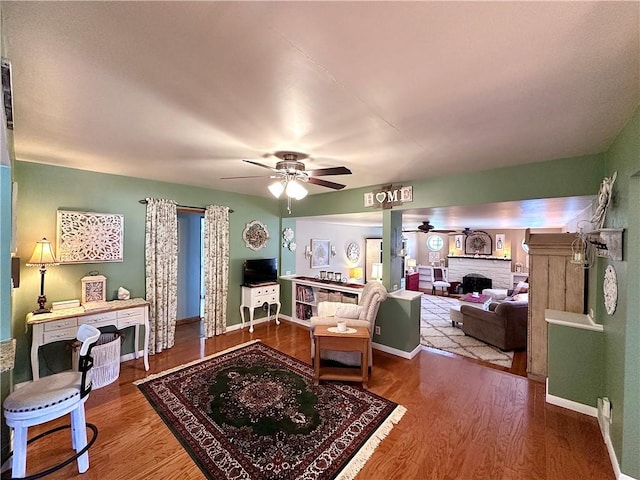 living room featuring a ceiling fan, wood finished floors, baseboards, and a fireplace