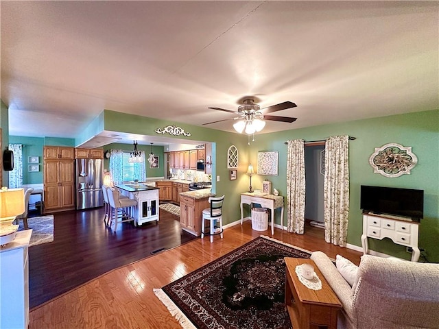 living area with a ceiling fan, dark wood-style flooring, and baseboards