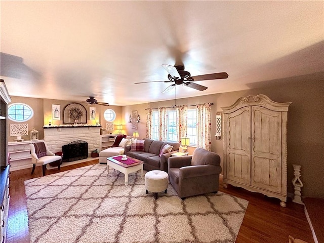 living area with a ceiling fan, a stone fireplace, and wood finished floors