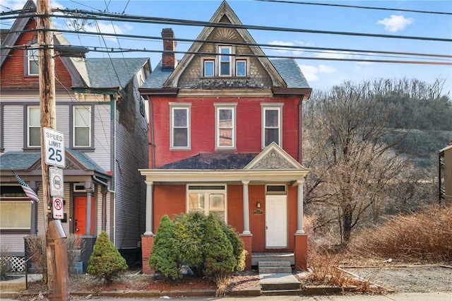 view of front of house with covered porch, brick siding, and a chimney