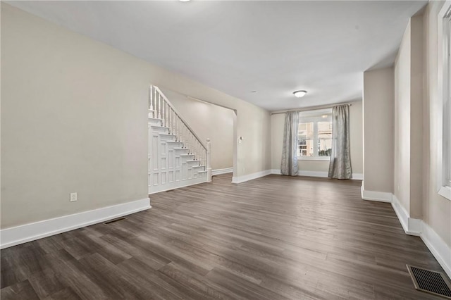 unfurnished living room with visible vents, baseboards, dark wood-type flooring, and stairway