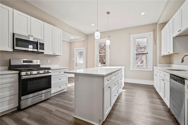 kitchen with dark wood-type flooring, a sink, a kitchen island, appliances with stainless steel finishes, and light countertops