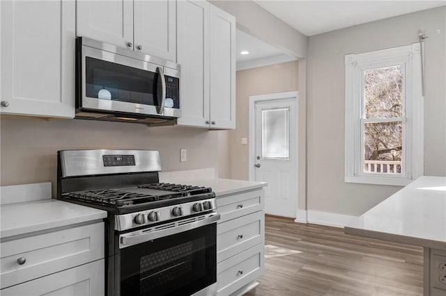 kitchen featuring baseboards, light wood-type flooring, light countertops, stainless steel appliances, and white cabinetry