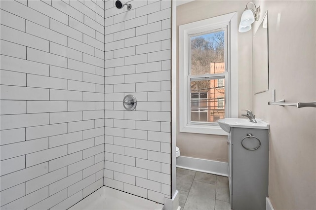 bathroom with toilet, tiled shower, vanity, and baseboards