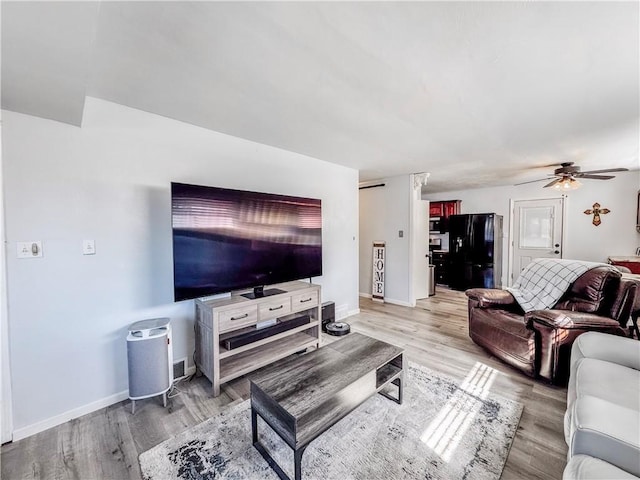 living room featuring light wood-style flooring, a ceiling fan, and baseboards