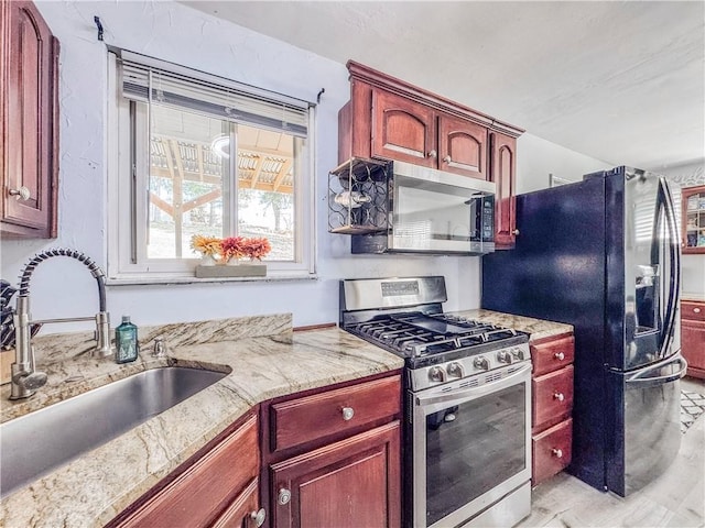 kitchen with light stone counters, dark brown cabinets, appliances with stainless steel finishes, and a sink