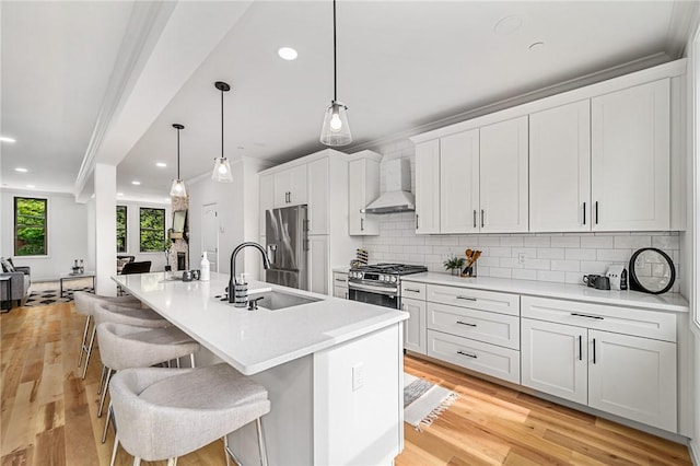 kitchen featuring a kitchen bar, light wood-type flooring, a sink, stainless steel appliances, and wall chimney exhaust hood