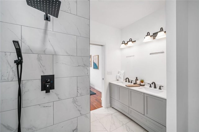 bathroom with double vanity, marble finish floor, tiled shower, and a sink