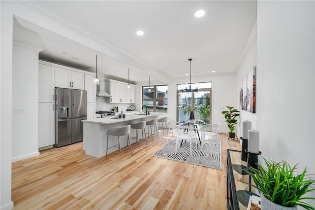 kitchen with light wood-style flooring, stainless steel fridge with ice dispenser, white cabinets, a kitchen breakfast bar, and a chandelier