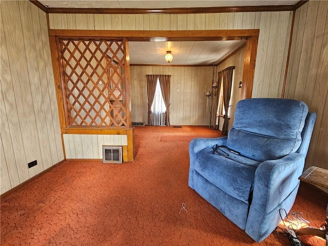 sitting room featuring wooden walls, visible vents, baseboards, ornamental molding, and carpet floors