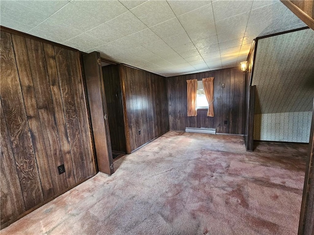 carpeted spare room featuring baseboard heating and wood walls