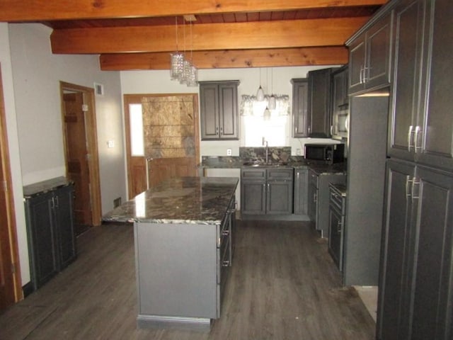 kitchen with dark wood finished floors, dark stone counters, stainless steel microwave, beamed ceiling, and a center island