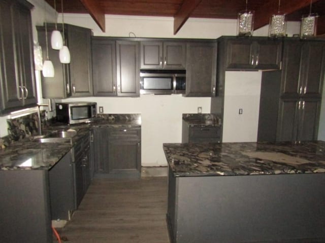 kitchen with stainless steel microwave, beamed ceiling, dark wood-style floors, and hanging light fixtures