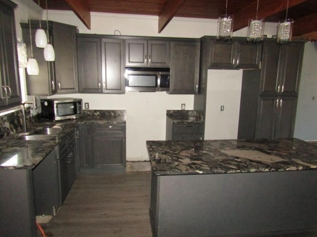 kitchen featuring a sink, stainless steel microwave, beam ceiling, and dark stone countertops