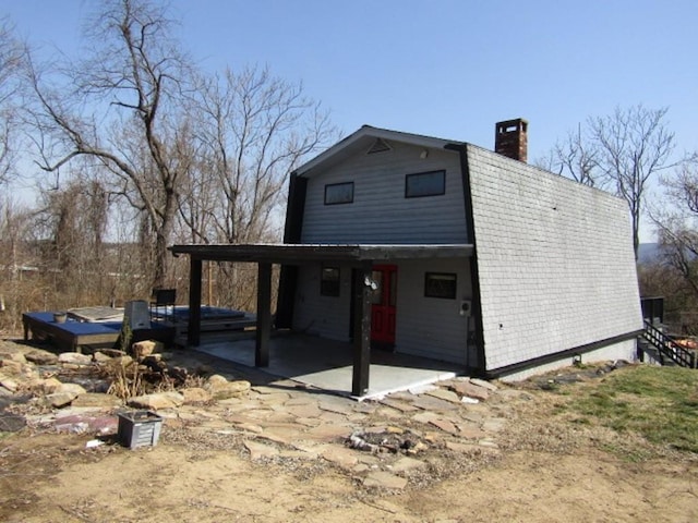 rear view of house with a gambrel roof, a patio, and a chimney