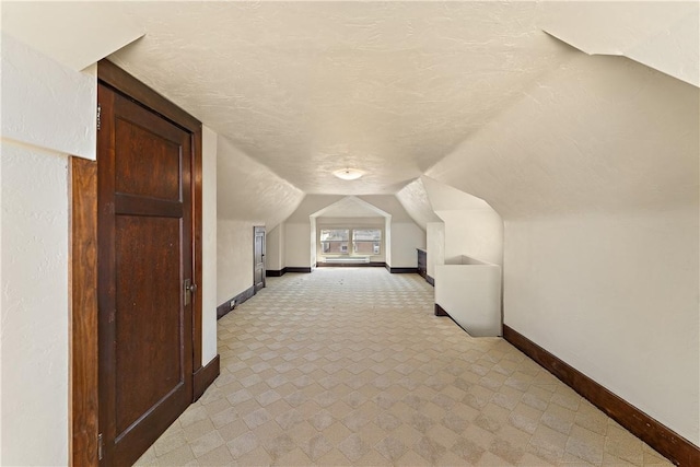 additional living space featuring vaulted ceiling, baseboards, and a textured ceiling