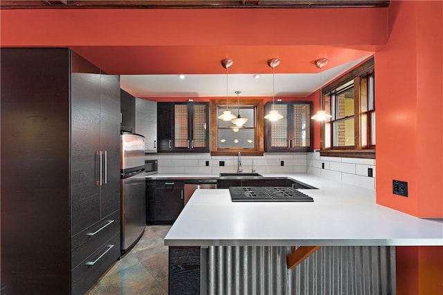 kitchen featuring a sink, backsplash, appliances with stainless steel finishes, a peninsula, and light countertops