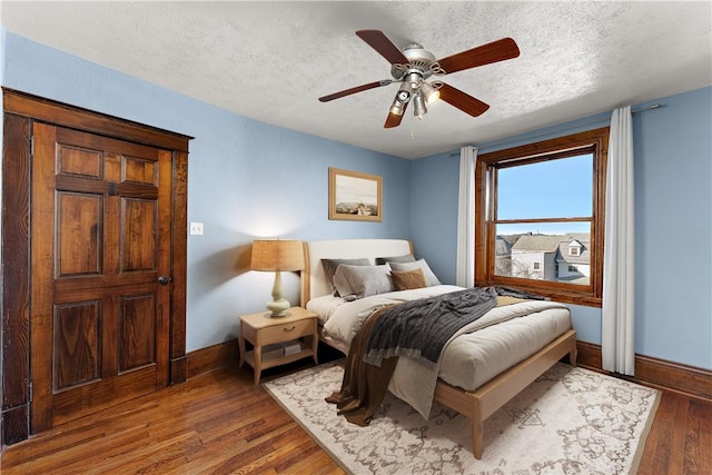 bedroom featuring ceiling fan, a textured ceiling, baseboards, and wood finished floors