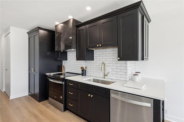 kitchen featuring wall chimney range hood, light countertops, decorative backsplash, appliances with stainless steel finishes, and a sink