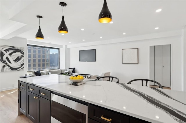 kitchen with light wood finished floors, stainless steel microwave, open floor plan, light stone countertops, and decorative light fixtures
