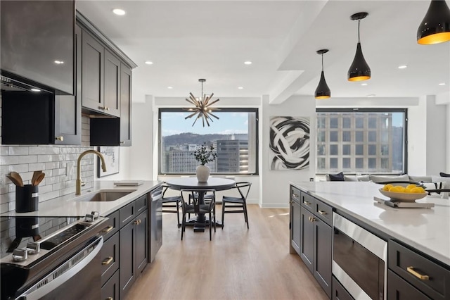 kitchen featuring tasteful backsplash, a sink, stainless steel appliances, light wood-style flooring, and decorative light fixtures
