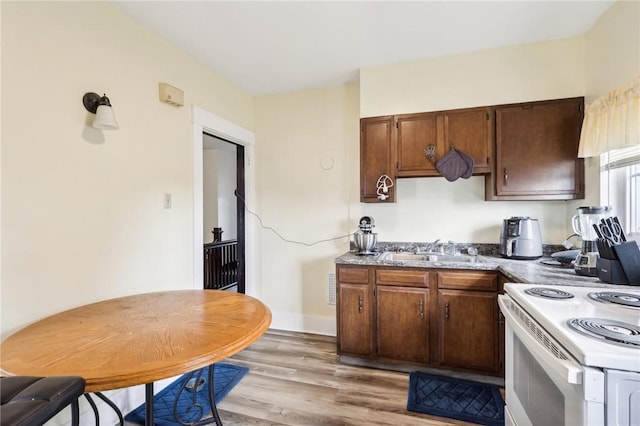 kitchen with baseboards, light wood-type flooring, white range with electric stovetop, and a sink