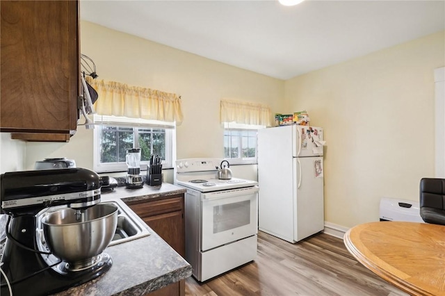 kitchen with white appliances, baseboards, a sink, light wood-style floors, and dark countertops