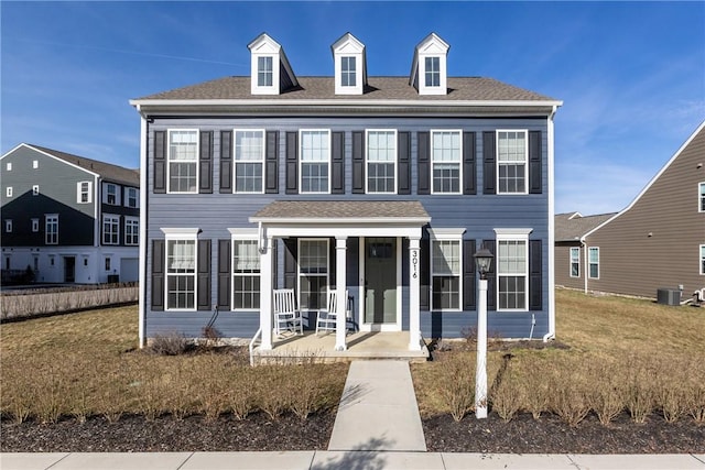 view of front of property with central air condition unit, covered porch, a shingled roof, and a front yard